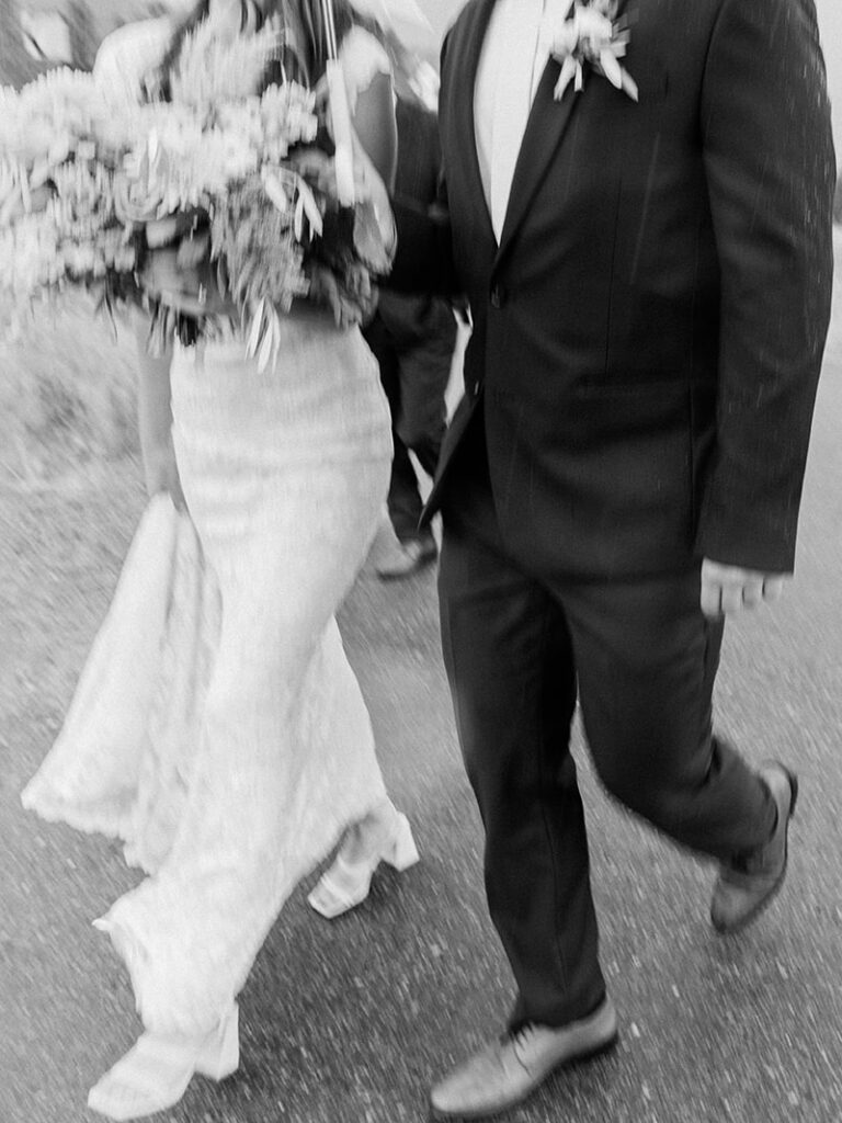 black and white photo of bride and groom walking on their wedding day 