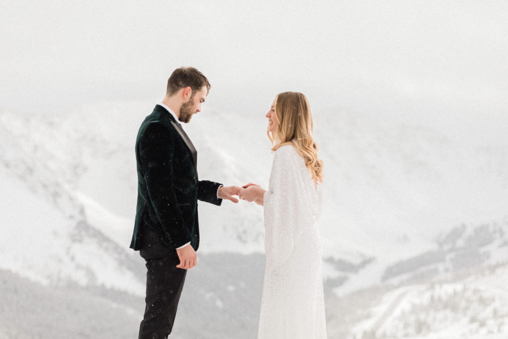 bride and groom exchanging rings and laughing during magical snowfall at the top of a mountain in colorado during elopement 