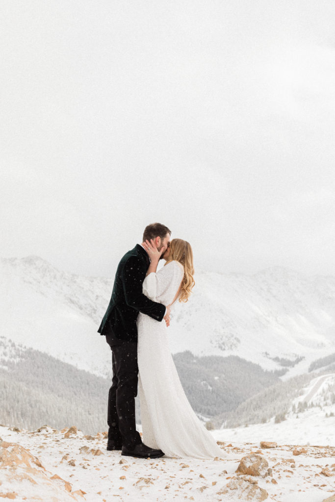 bride and groom kiss during magical snowy mountain white winter elopement at the top of loveland pass colorado 