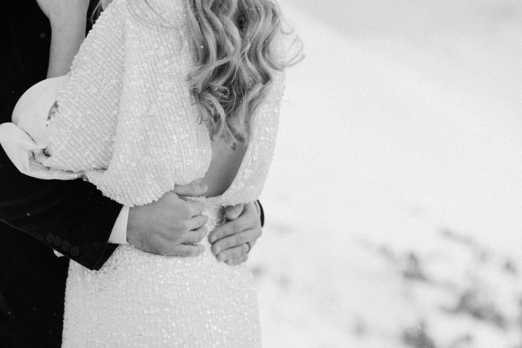 black and white close up shot of grooms hands around the brides waist during magical snowy mountain white winter elopement at the top of loveland pass colorado 