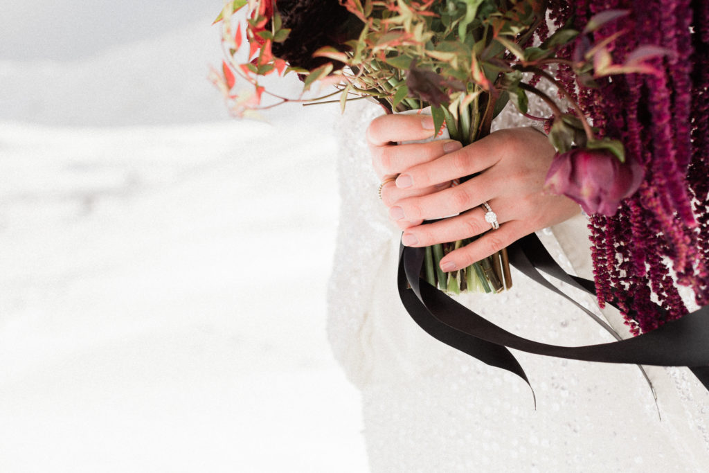 close up of brides engagement and wedding ring as she holds her deep red wedding bouquet from denver colorado florist project floral