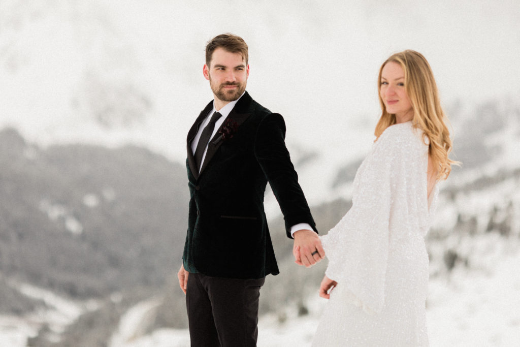 couple eloping at Loveland Pass in Colorado during the winter, bride and groom holding hands and walking in snow while looking at the camera