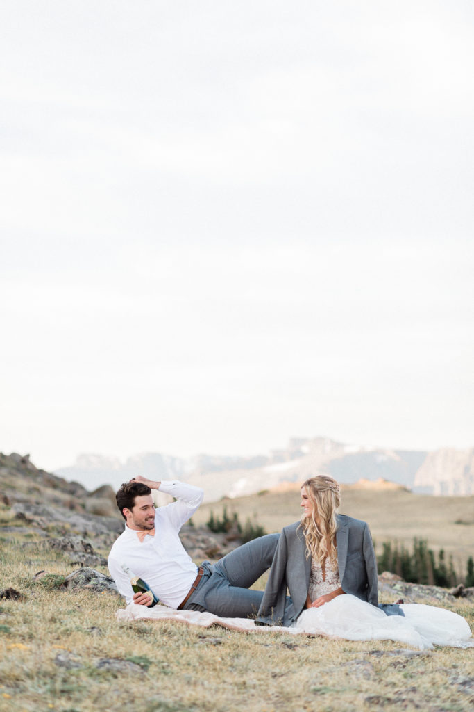 groom brushes his hair back while bride and groom celebrate their marriage with a bottle of champagne during first look on Trail Ridge Road Sunrise Elopement in Rocky Mountain National Park RMNP by Diana Coulter