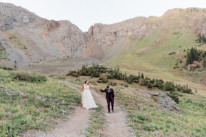 Illinois couple eloped in Telluride, Colorado bride holding grooms hand while walking along dirt path in the mountains groom in maroon suit near Alta Lakes for stunning sunrise elopement with Diana Coulter