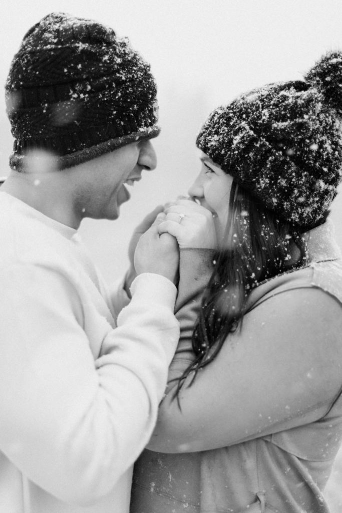 sweet engagement session during a snowstorm while groom warms up the bride’s hands and kisses them during their snowy Boulder engagement session with the Colorado Rocky Mountains behind them with Colorado wedding photographer Diana Coulter