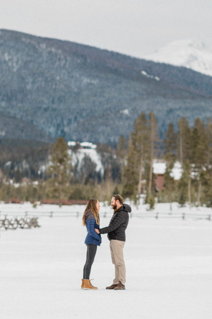boyfriend holding girlfriends waist getting ready to propose to her on new years eve they are wearing jackets and standing in the snow at devils thumb ranch in tabernash, colorado wearing patagonia and sorels