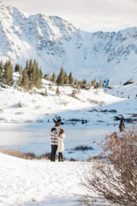 man about to propose to woman, standing on a snowy mountaintop ready to say yes