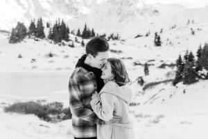 Blurry B+W black and white photo of newly engaged couple kissing and laughing and enjoying each other on top of a snowy mountain in Breckenridge, Colorado