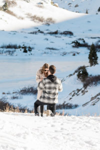 man down on one knee proposing, standing on a snowy mountaintop at loveland pass in Colorado and woman says yes! 