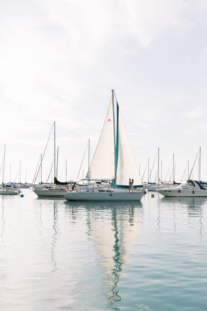 A wide view of a couple during their summer engagement session in Chicago while on a sailboat at the Lake Michigan Harbor.