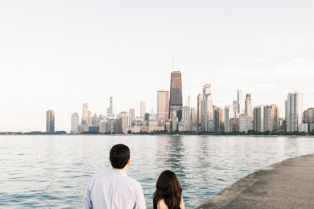 back of the couple facing the Chicago skyline during their engagement session in the summer with a view from Oak Street Beach